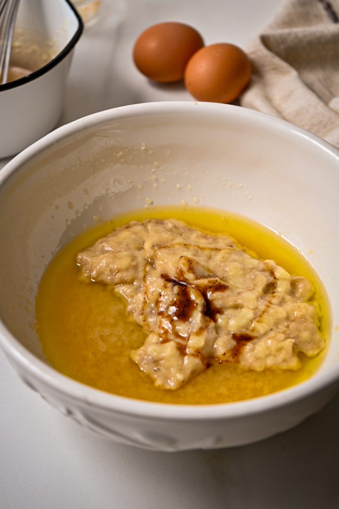 Mashed banana with melted butter and vanilla in a mixing bowl.