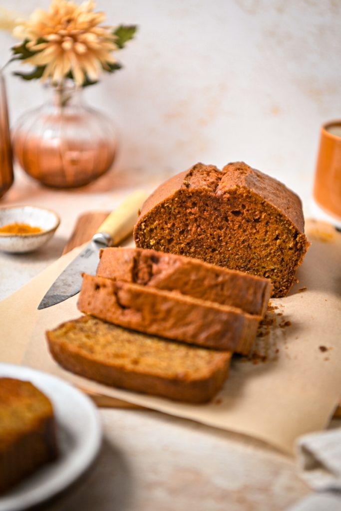Golden milk banana bread on a wooden board with some slices off the end.