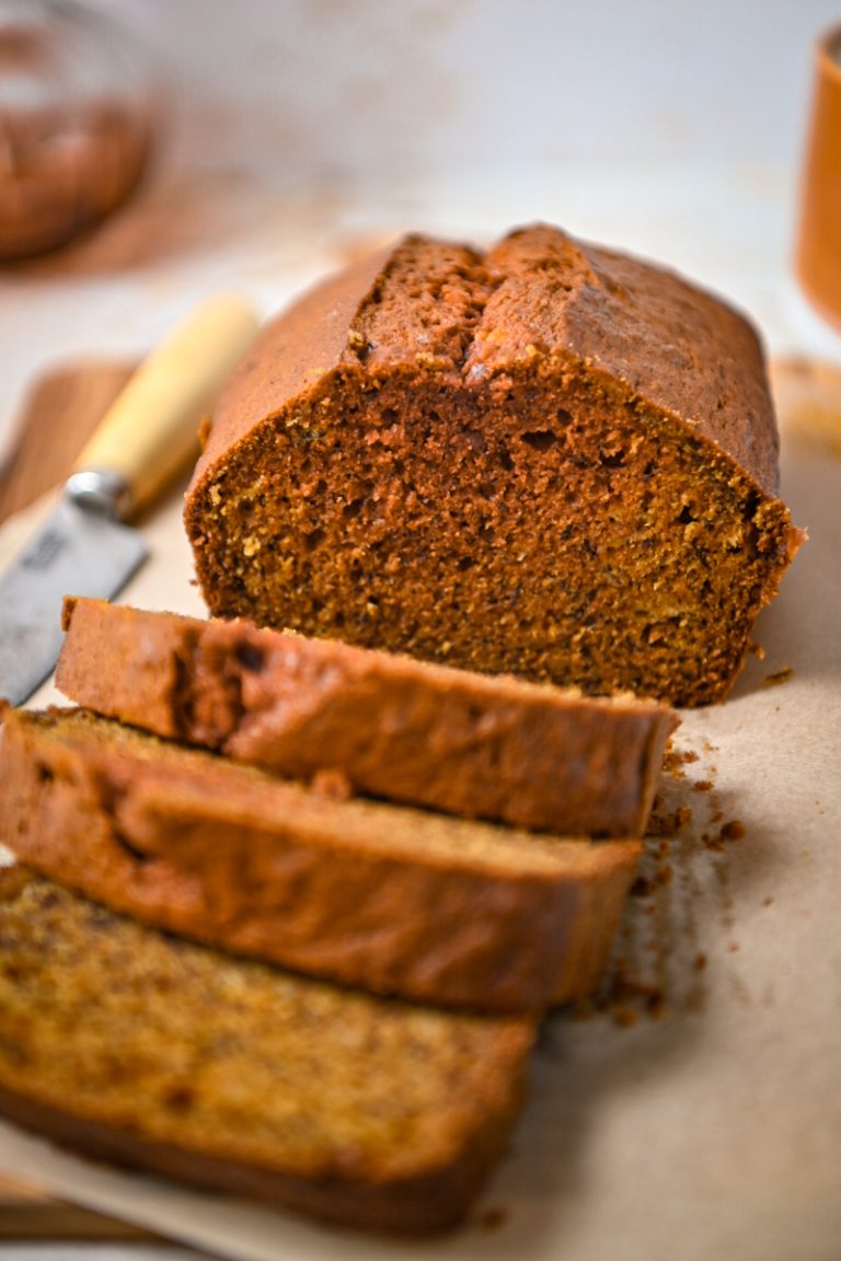 Close up of golden milk banana bread on a wooden board with some slices off the end.
