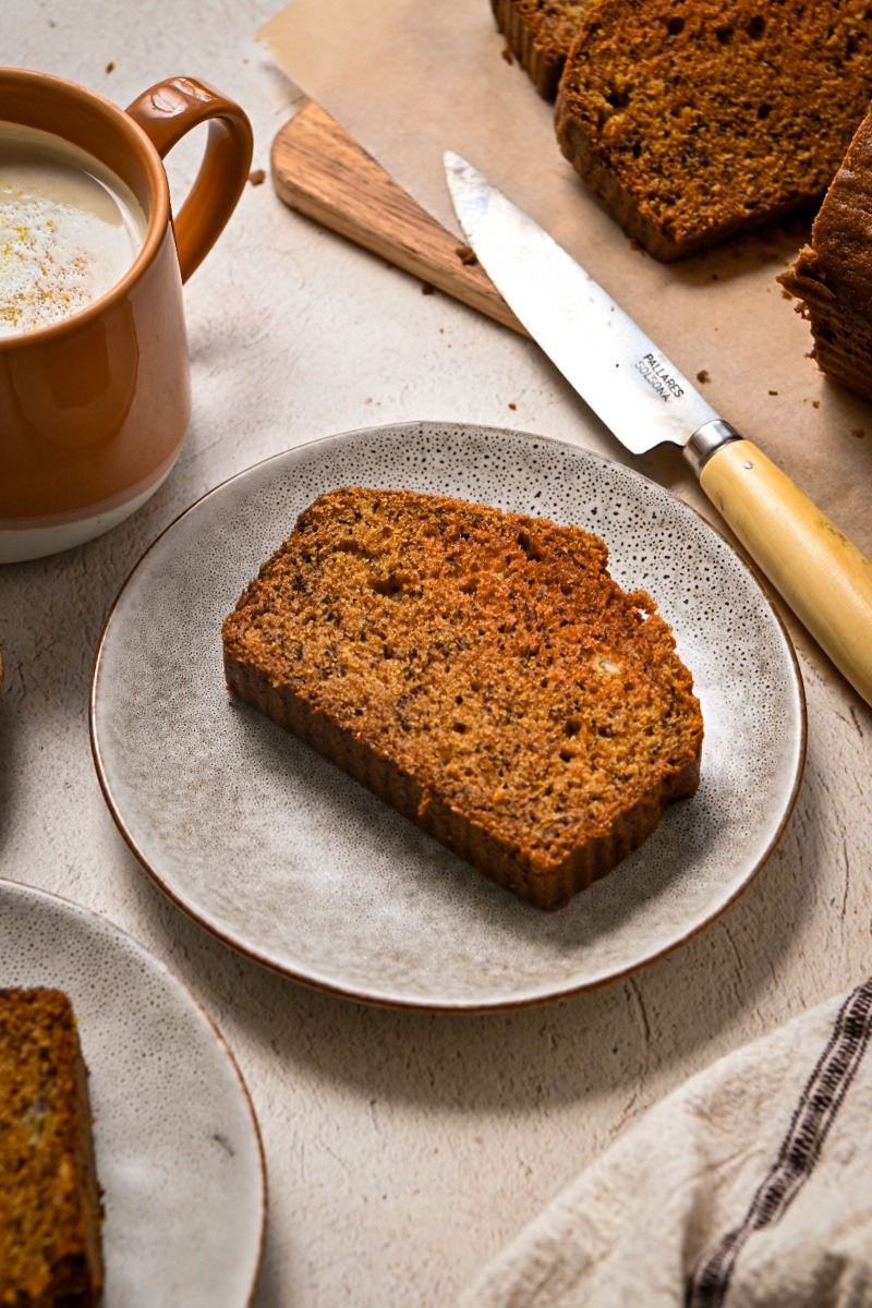 Slice of golden milk banana bread served on a plate next to a mug of coffee.