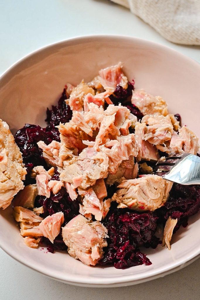 Tuna added to shredded beets in a bowl.