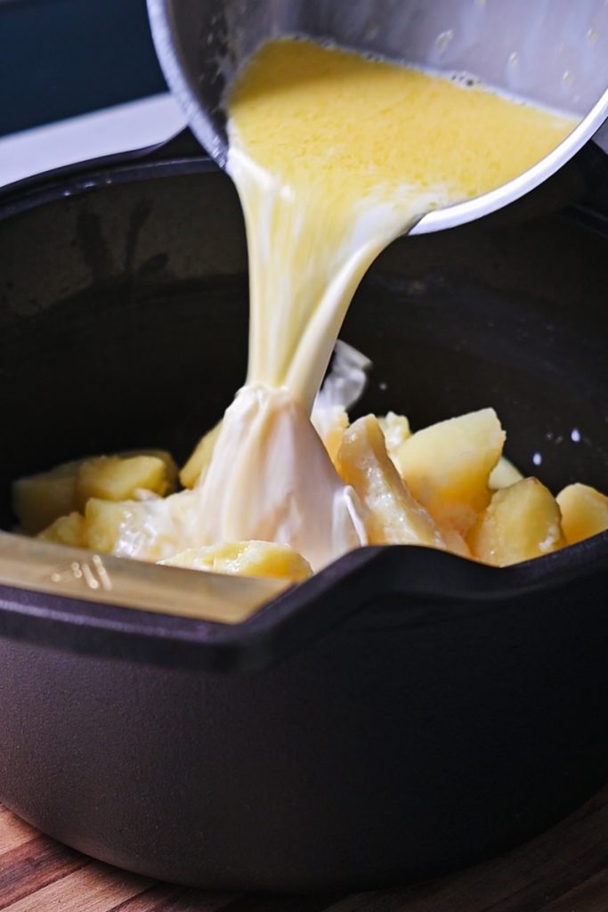 Pouring the butter and cream mixture over the potatoes in a pot.