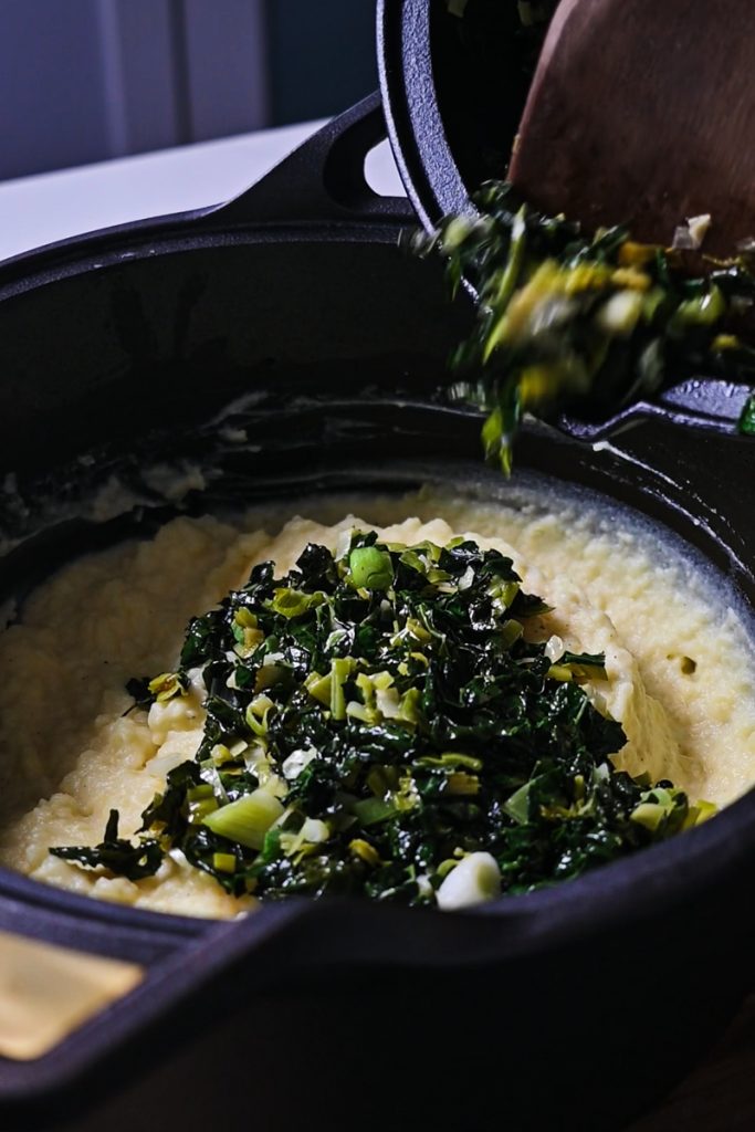 Kale and leeks added to the mashed potatoes in a pot.