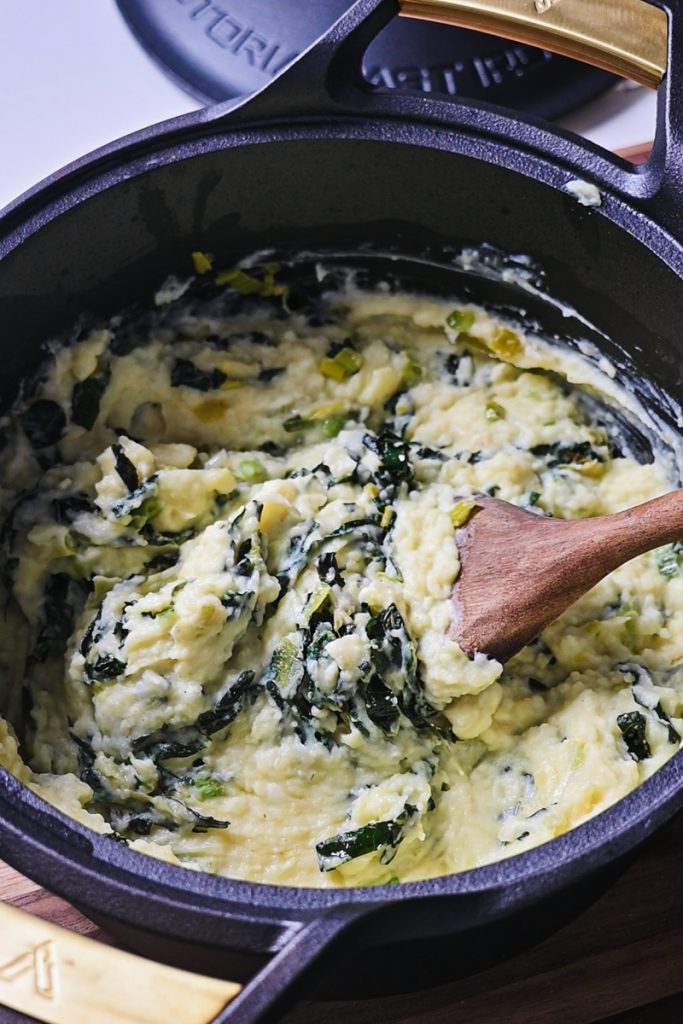 Wooden spoon stirring the Irish colcannon in a large Dutch oven pot.
