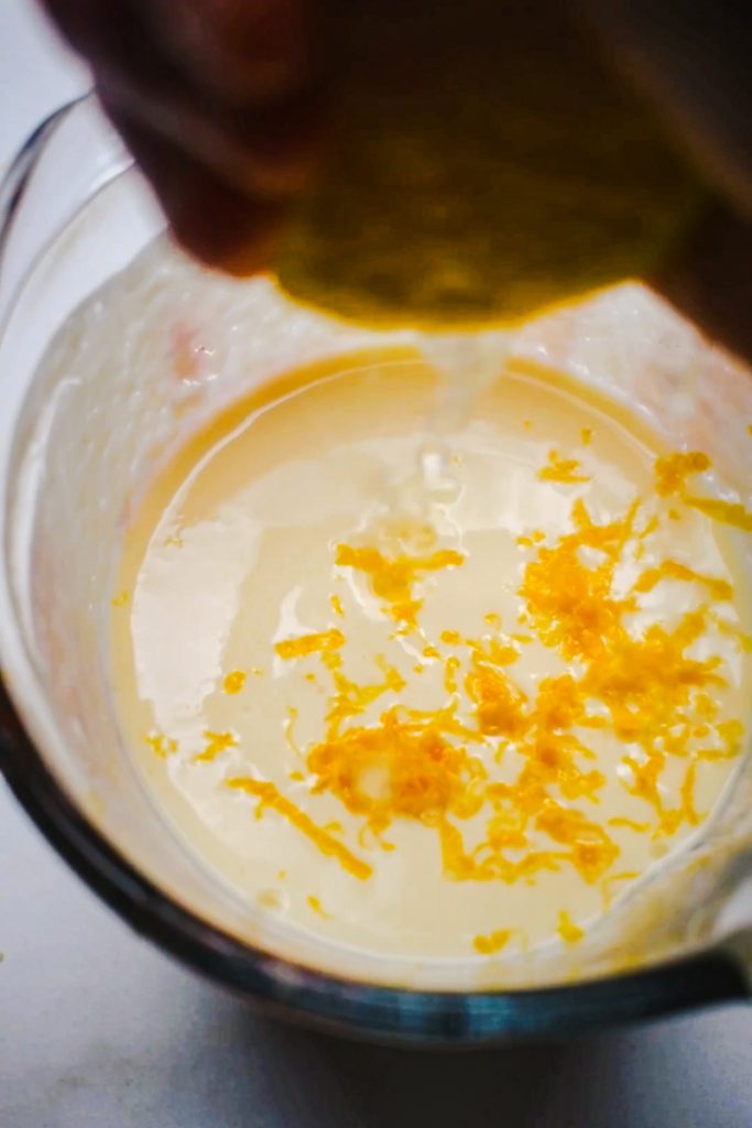 Lemon juice being squeezed into a measuring cup of lemon zest, yogurt, and egg.