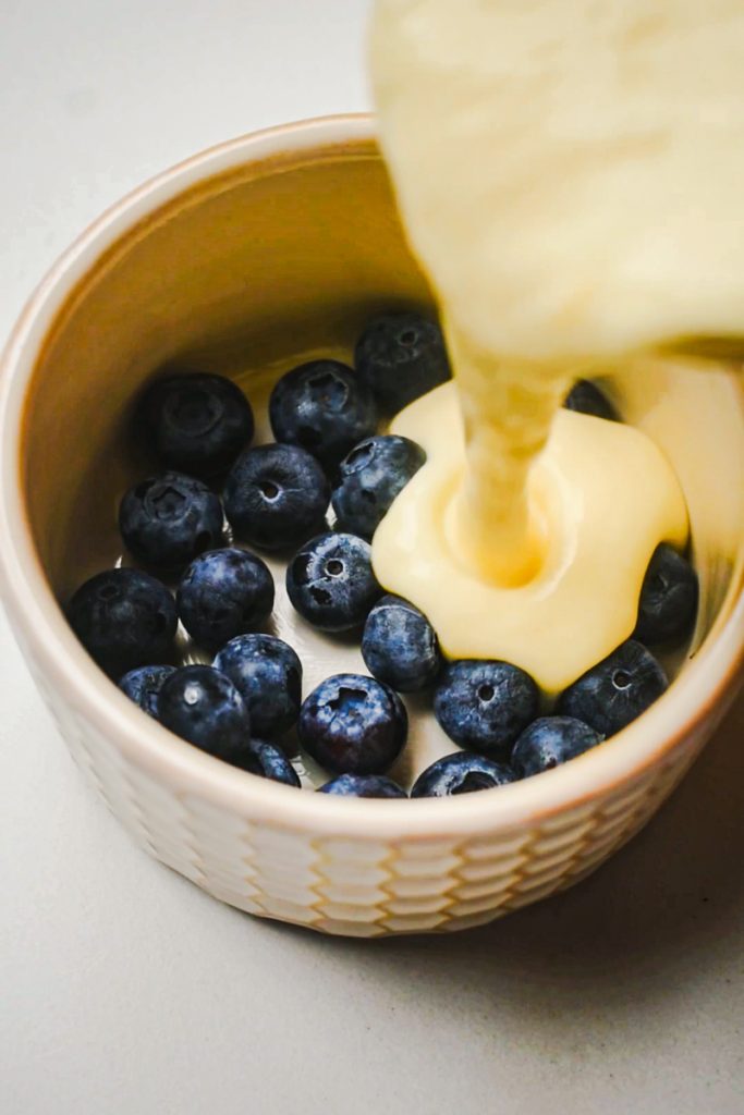 Blueberries in a ramekin with the yogurt mixture being poured over it.