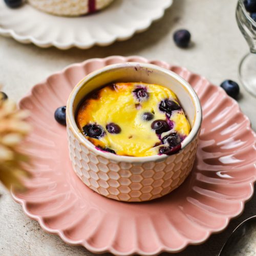 Berry baked yogurt in a ramekin which is on a pink plate.