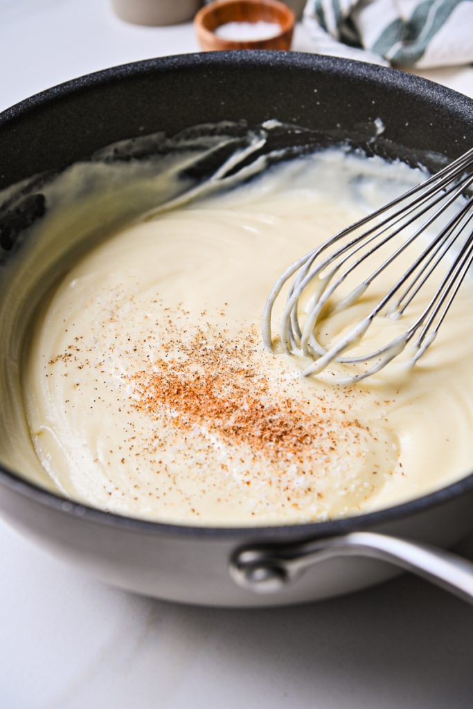 Nutmeg added to creamy sauce in a skillet.