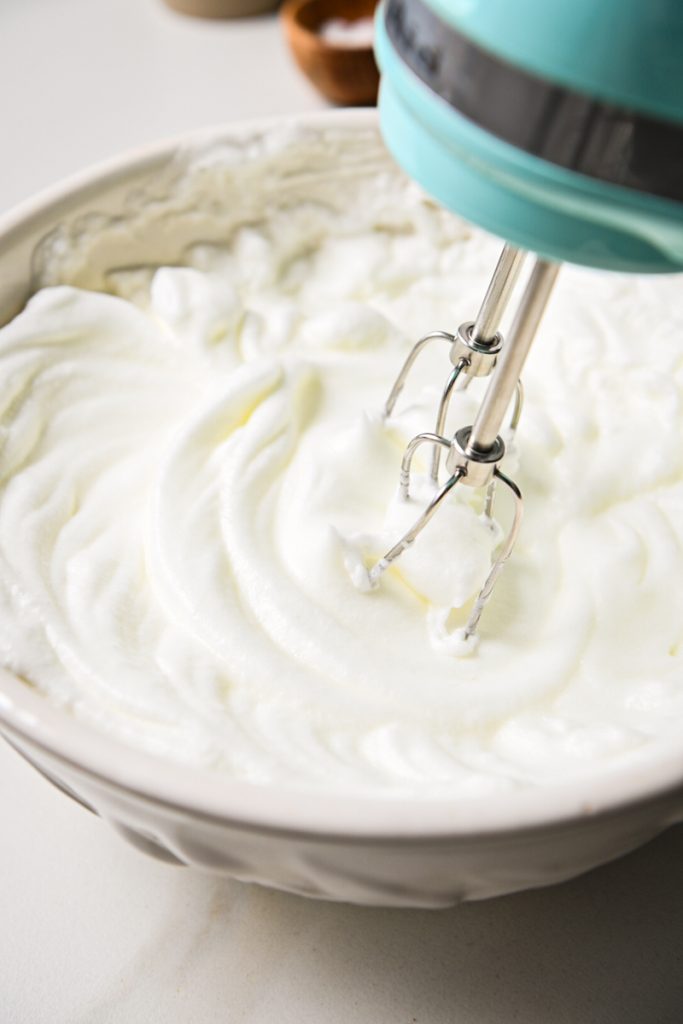 Whipping egg whites in a large mixing bowl with a hand mixer.