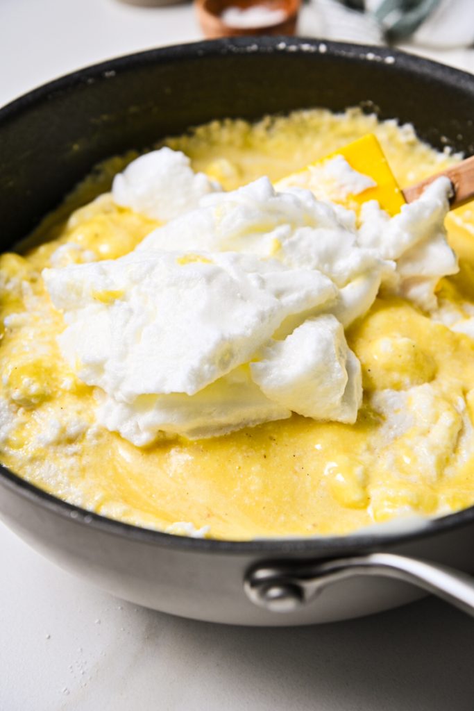 Folding in the egg whites into the cheesy mornay sauce in a skillet.