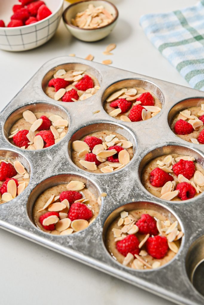 Raspberries and sliced almonds placed on top of financier batter in a muffin tin.