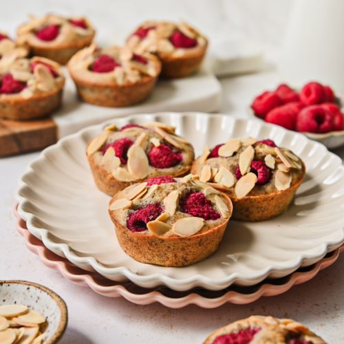 Side view of financier muffins on a plate all topped with raspberries and almonds.