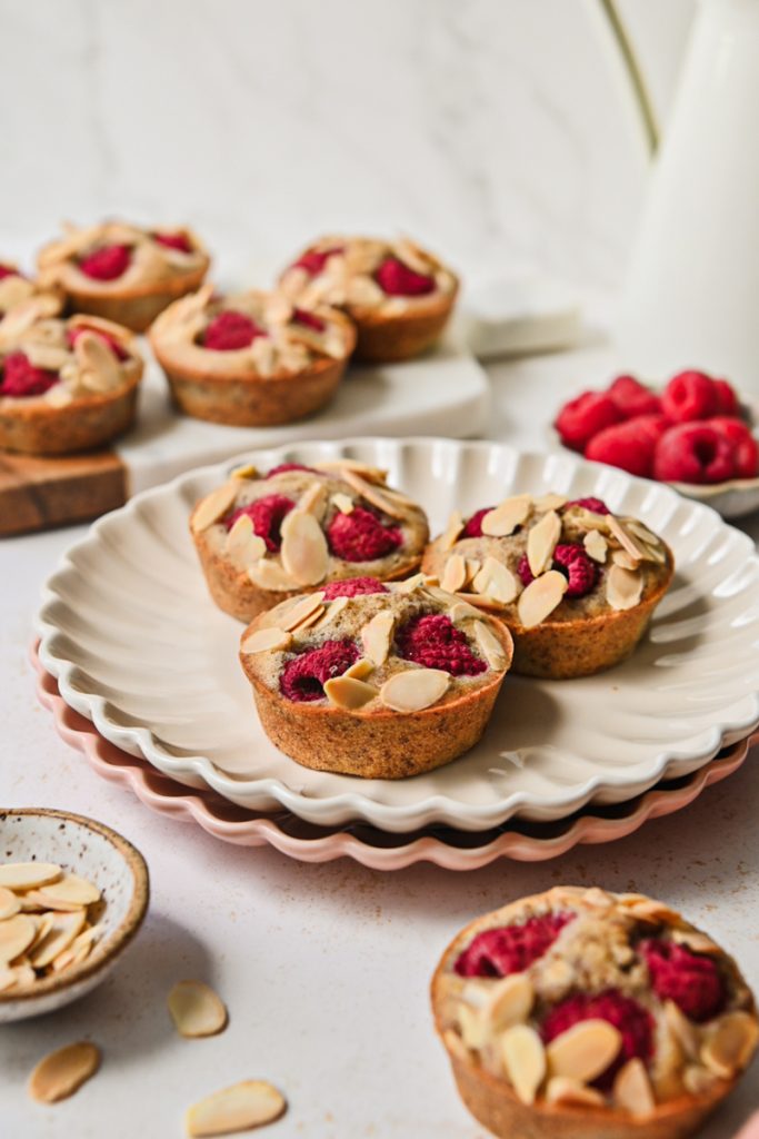 Side view of financier muffins on a plate all topped with raspberries and almonds.