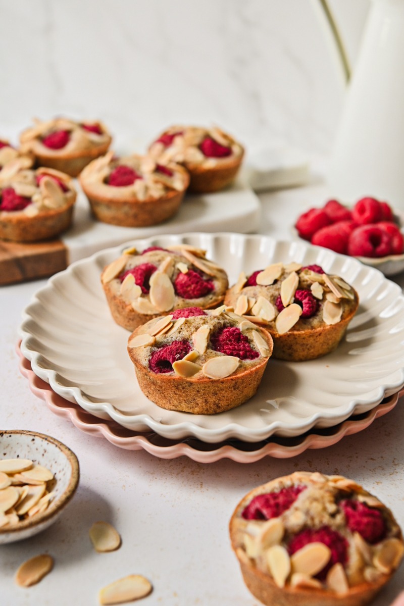 Side view of financier muffins on a plate all topped with raspberries and almonds.