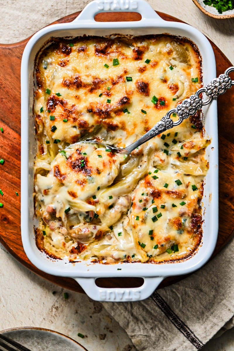 Fennel gratin with pancetta in a white baking dish with a serving spoon.