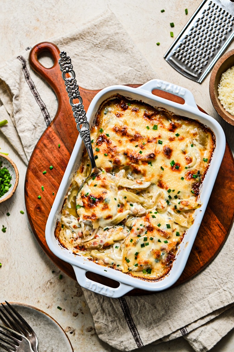 Overhead shot of creamy fennel gratin in a white baking dish on a wooden board.