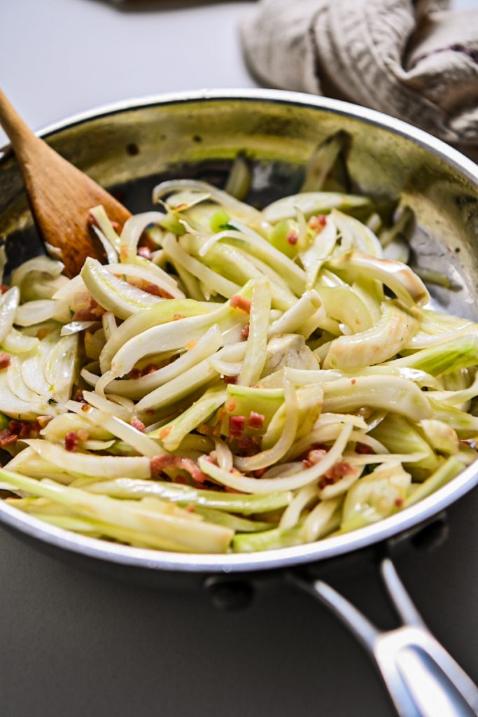 Sliced fennel and onions added to the pancetta in a skillet.