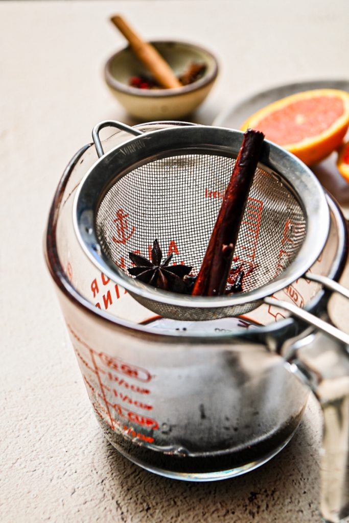 Mulled wine strained over a fine mesh strainer into a measuring cup.