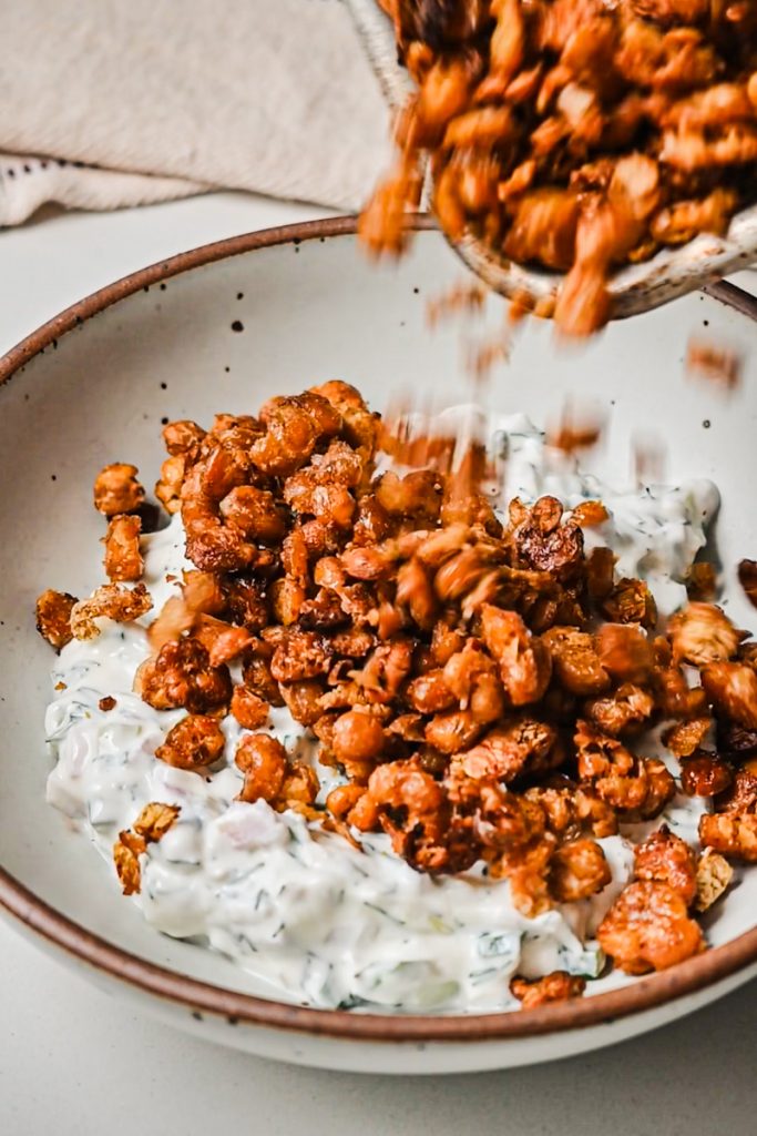 Crispy smashed chickpeas being added to the yogurt dressing in a bowl.