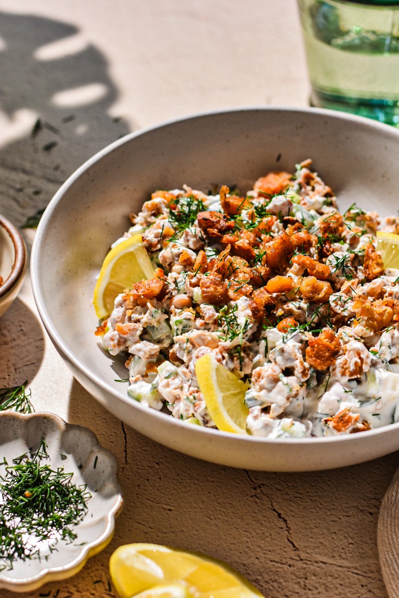Side view of a crispy smashed chickpea salad in a bowl with lemon slices.