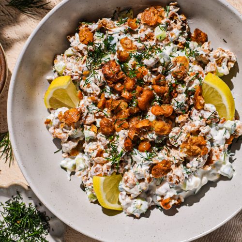 Smashed chickpea salad in a bowl with with dill and lemon slices on the side.