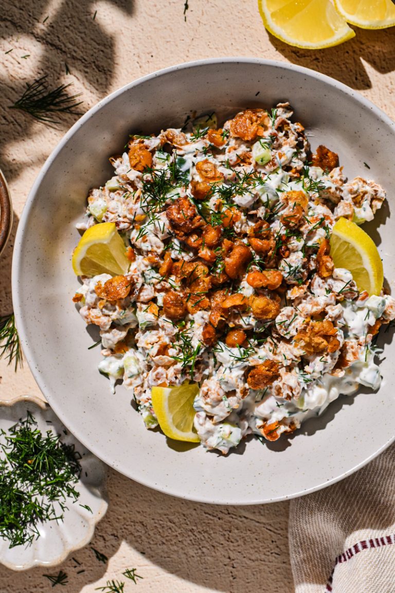 Smashed chickpea salad in a bowl with with dill and lemon slices on the side.