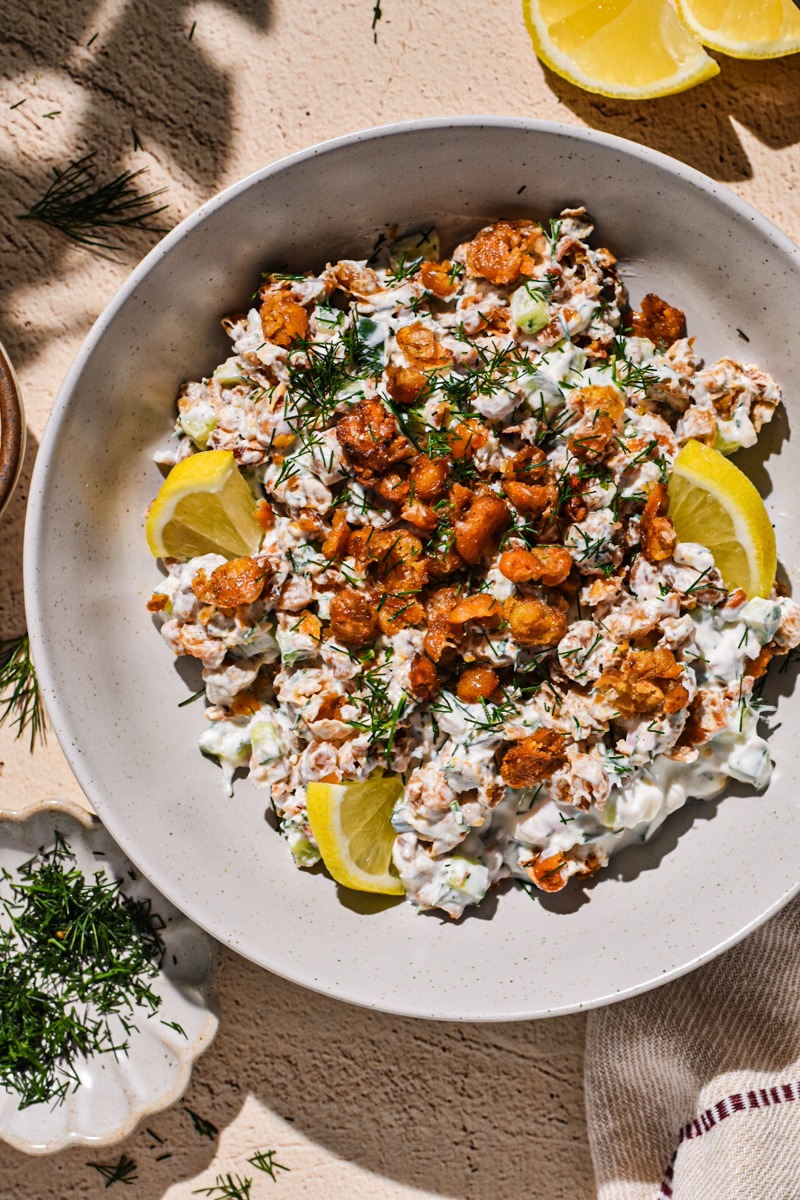 Smashed chickpea salad in a bowl with with dill and lemon slices on the side.