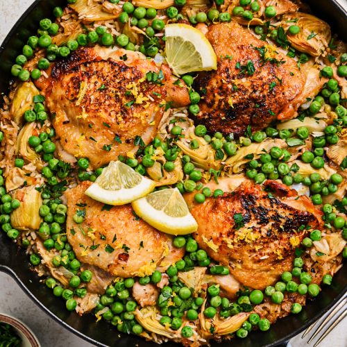 One pan lemon chicken and rice in a cast iron skillet with peas and artichokes.