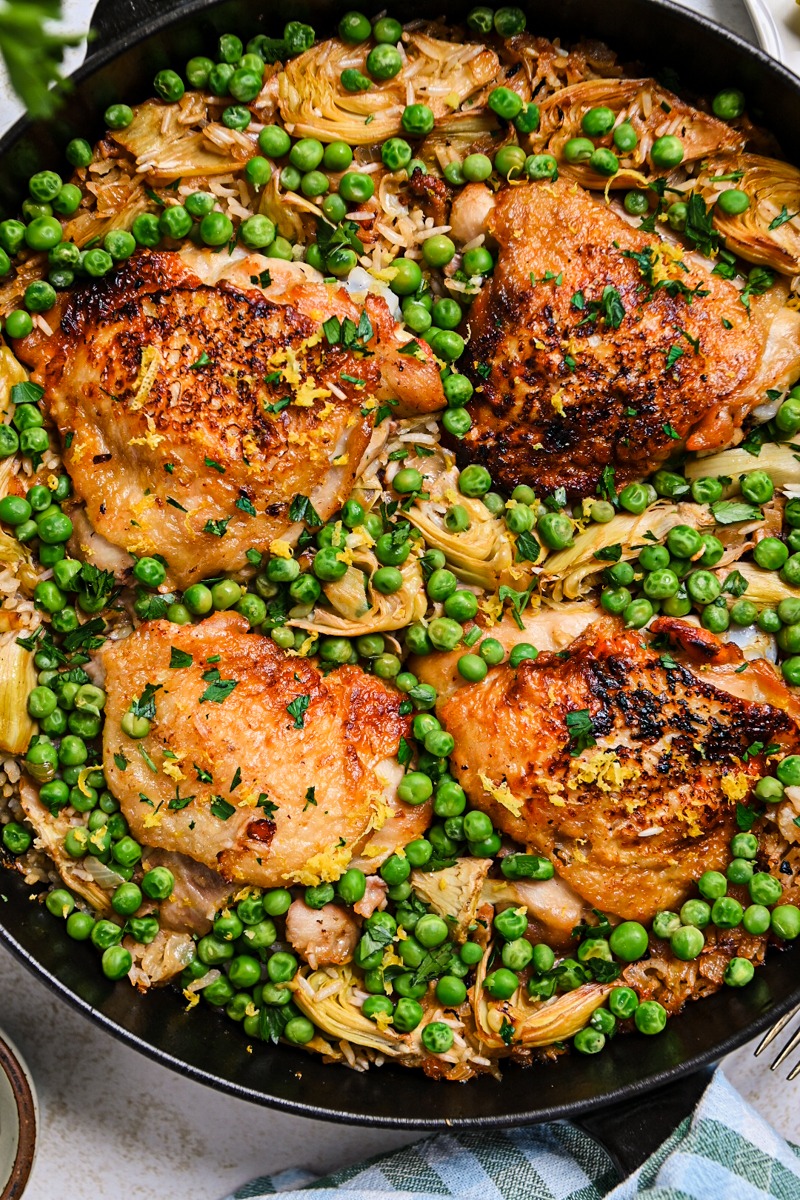 Close up of one pan lemon chicken and rice with peas and artichokes in a cast iron skillet.