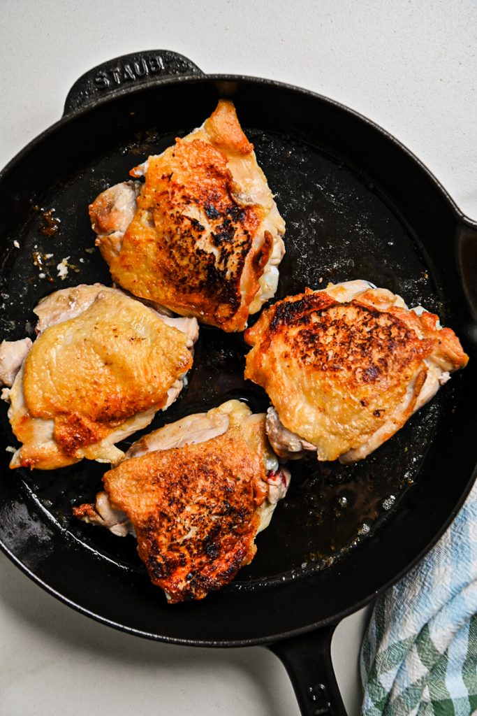 Chicken thighs searing in a cast iron skillet.