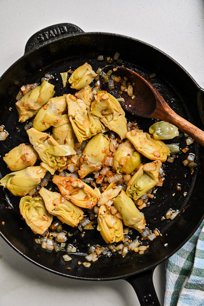 Artichokes, onions and garlic sautéing in a skillet.