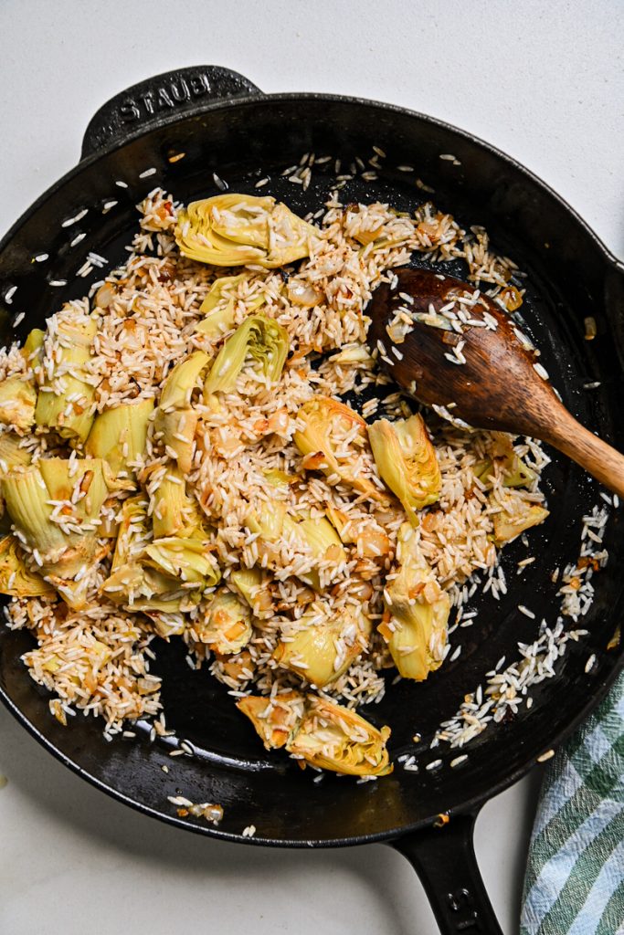 Rice added to the artichoke mixture in a skillet.