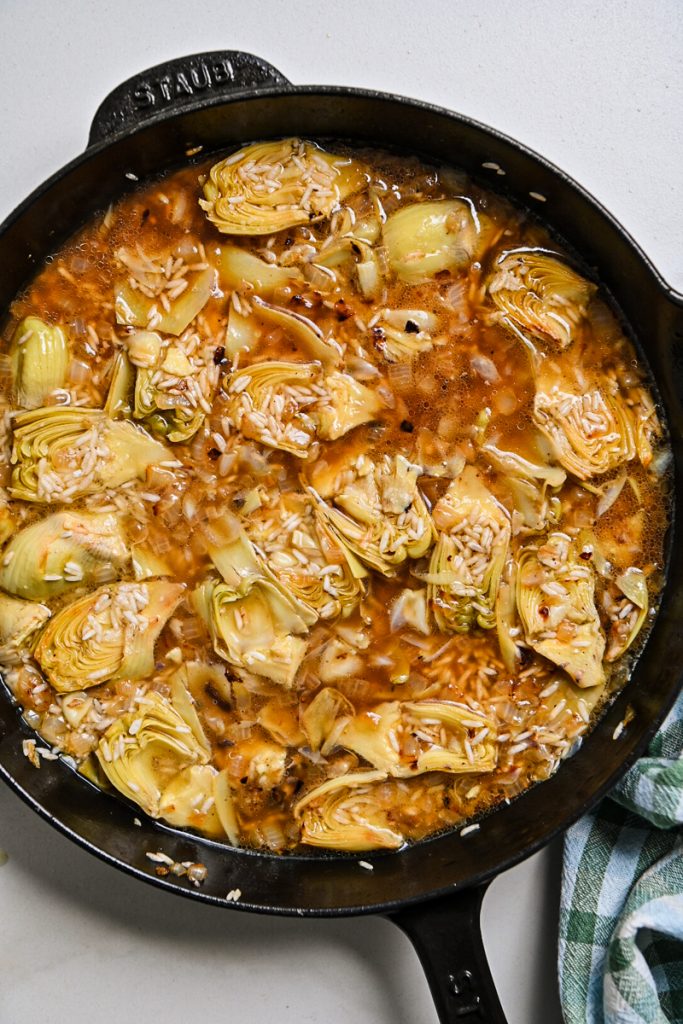 Broth added to the rice and artichoke mixture in a skillet.