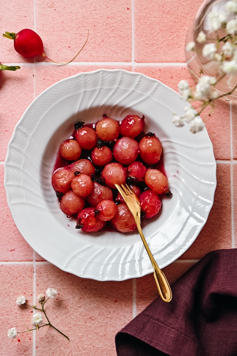 Overhead shot of glazed radishes in a white bowl with a golden fork.