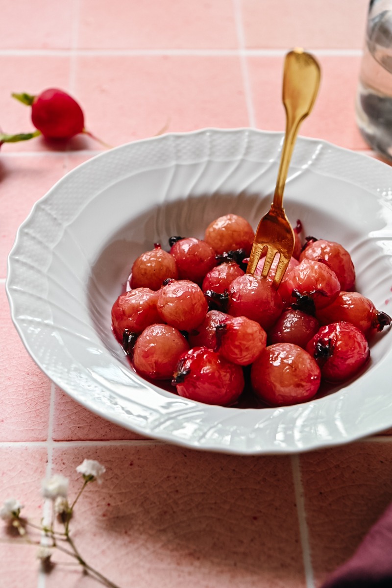 Side view of glazed radishes in a bowl with a fork sticking in one of them.