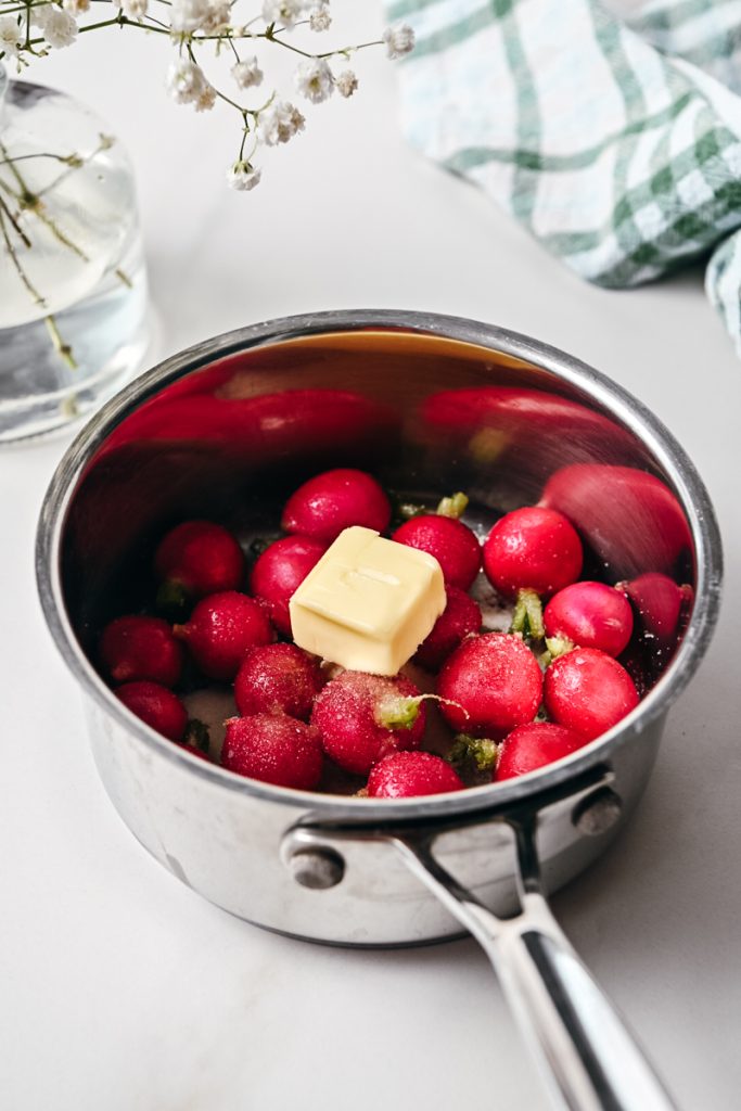Butter added on top of the sugar and radishes in a pan.