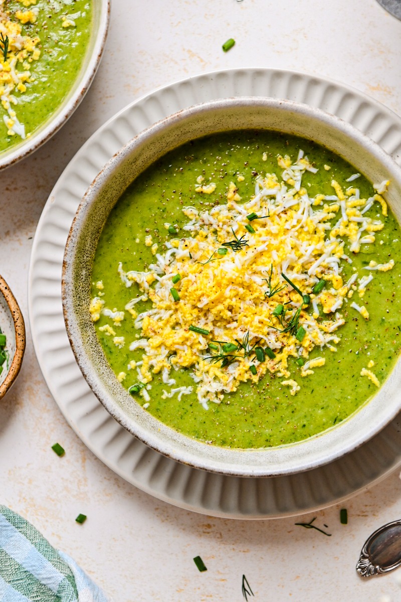 Overhead shot of green soup in a bowl garnished with boiled eggs and herbs.