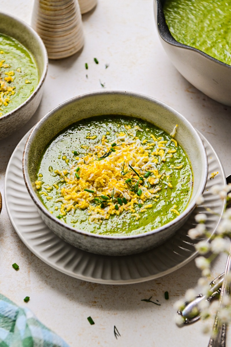 Side view of a bowl of green soup garnished with grated eggs.
