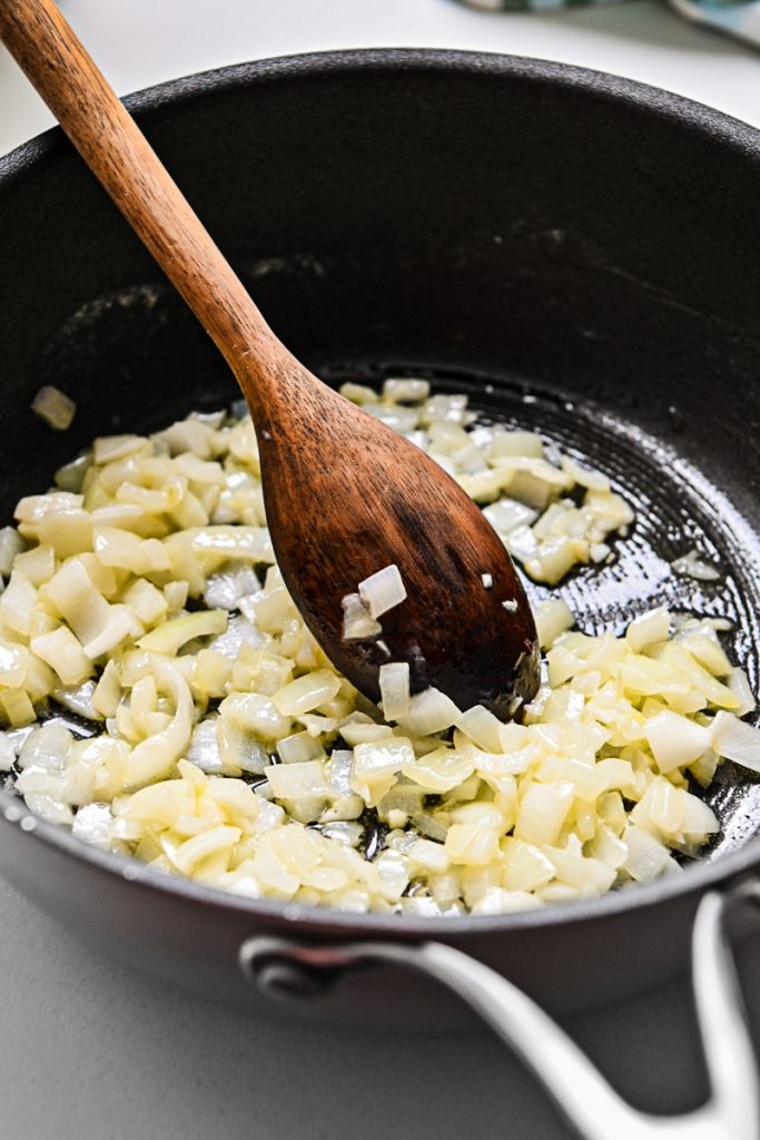 Onion sauteing in a skillet with a wooden spoon.