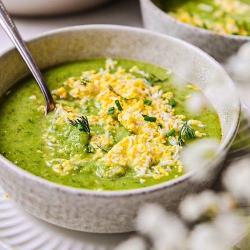 Side view of green soup in a bowl with grated eggs on top.