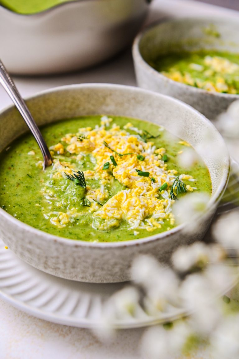 Side view of green soup in a bowl with grated eggs on top.