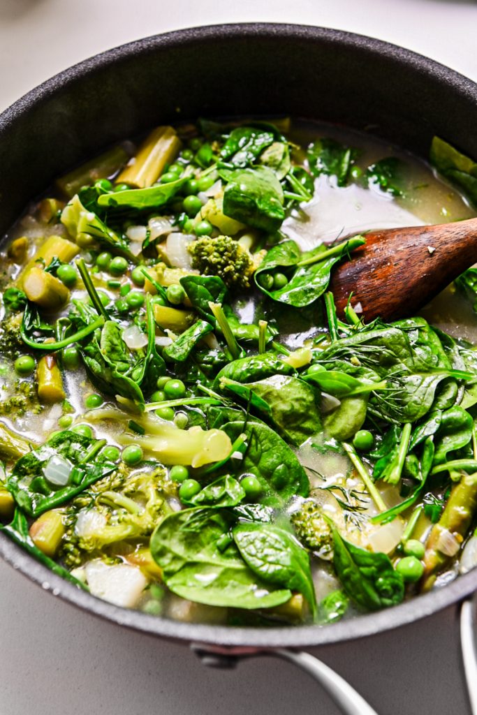 Spinach, peas, and herbs added to the skillet to cook.