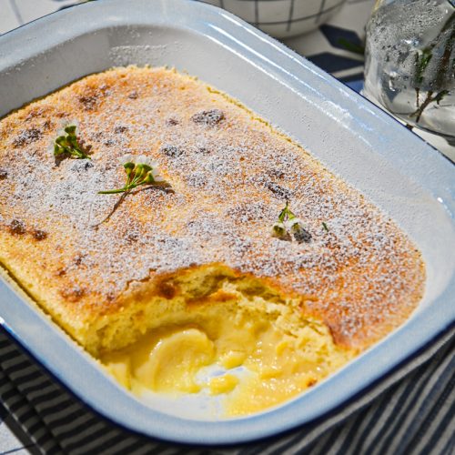 Side view of lemon pudding baked in a baking dish with a portion missing from the corner.