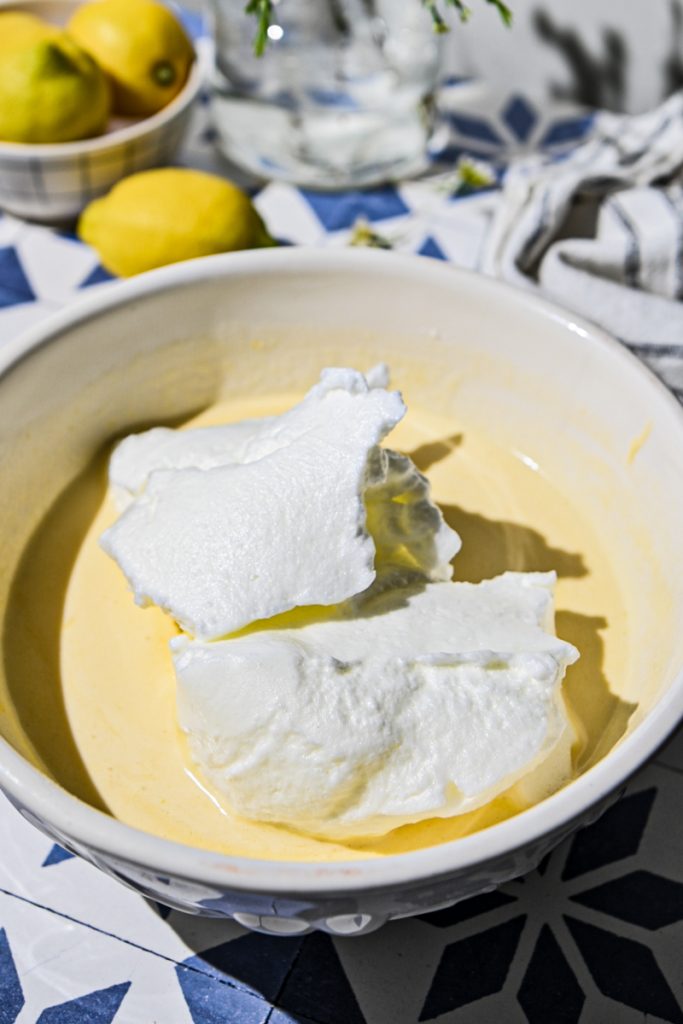 Whipped egg whites added to the lemon cake batter in a bowl.