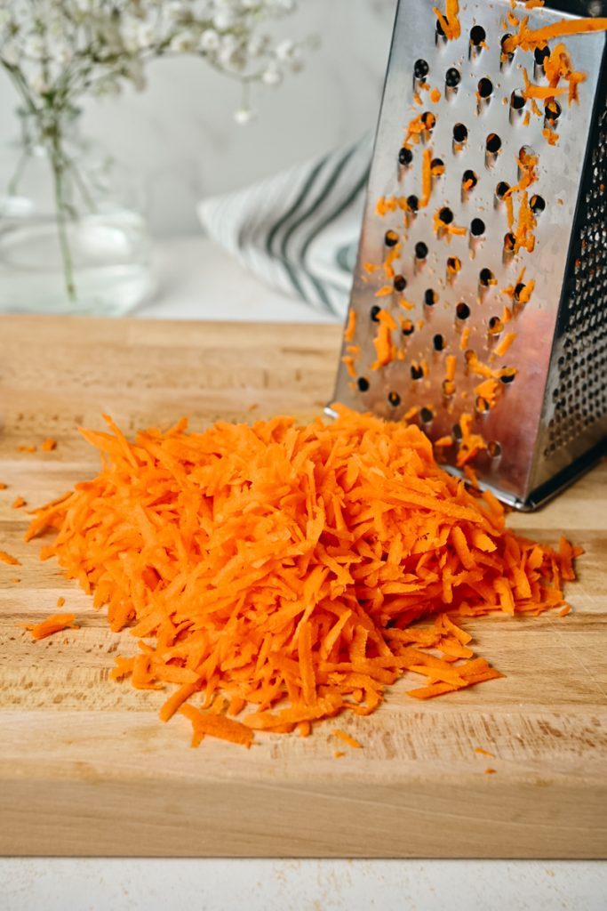 Shredded carrots on a table next to a grater.