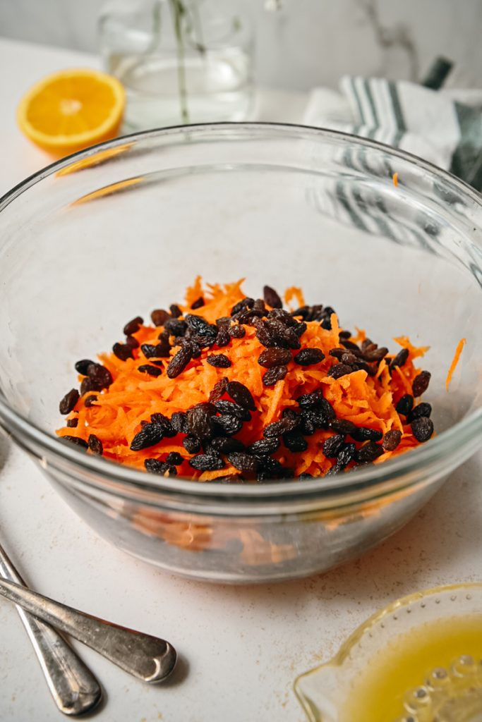 Raisins added to the shredded carrots in a bowl.
