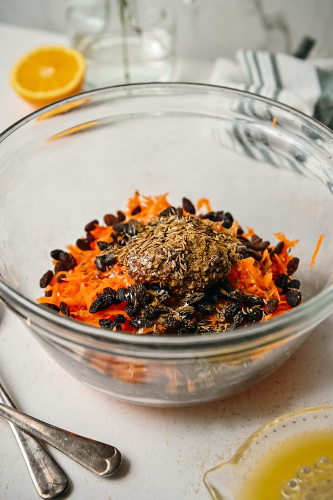Spices added to the carrots and raisins in a bowl.