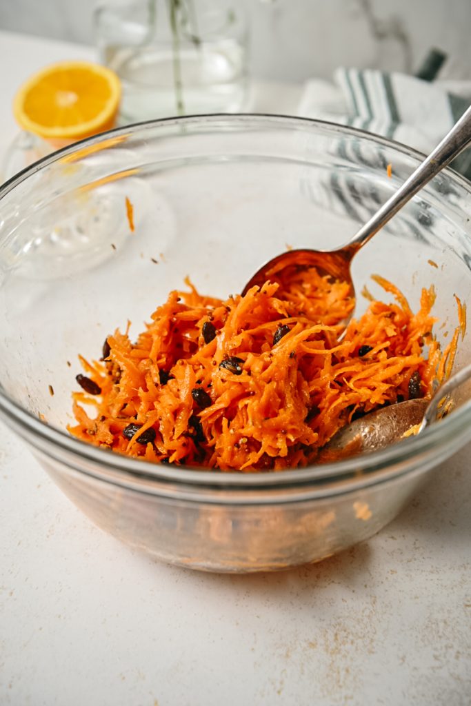 Two spoons stirring the Moroccan carrot salad in a bowl.