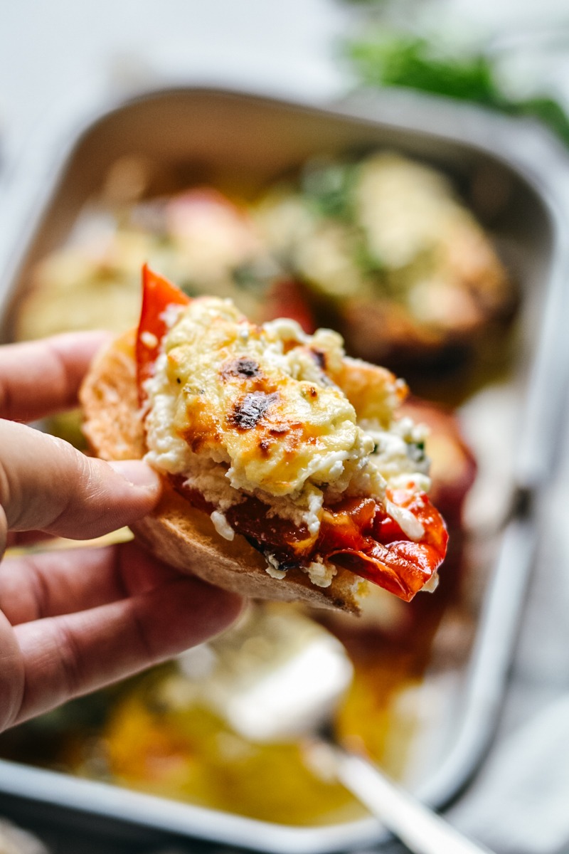 Hand holding a piece of bread with pepper and ricotta mixture on it.