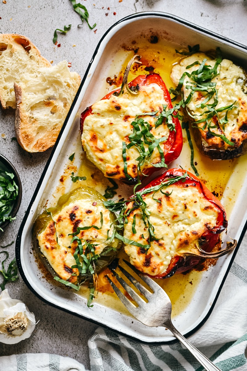 Roasted ricotta stuffed peppers in a baking dish with a serving fork in the dish.
